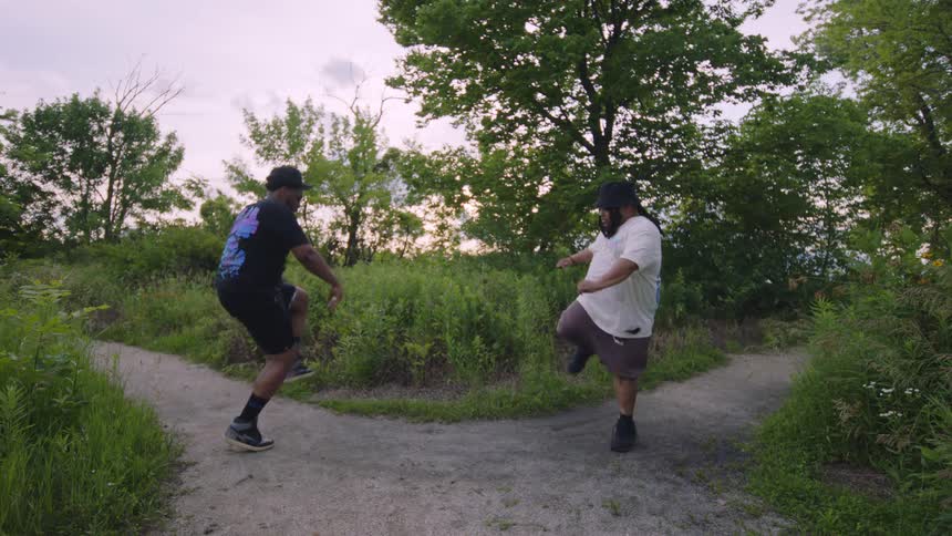 Two friends playfully dance together in slow motion on a nature trail at dusk