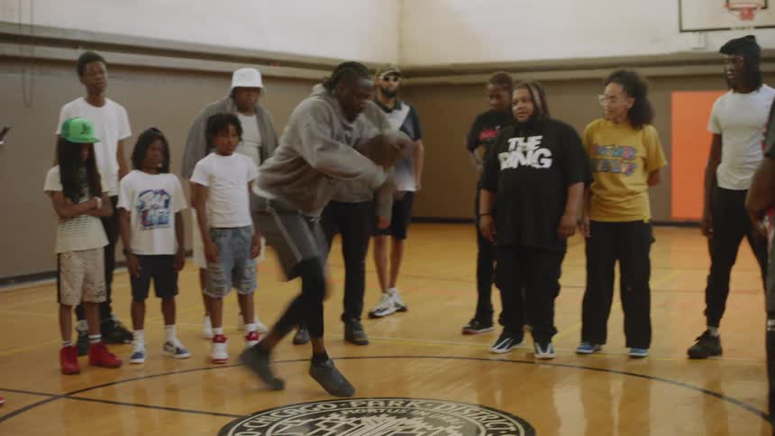A talented dancer showcases energetic street dance moves for an audience of kids and adults on a basketball court