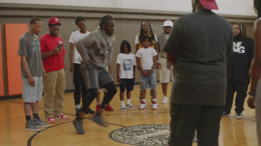 A talented man performs a fast-paced street dance for a crowd of onlookers in a gymnasium