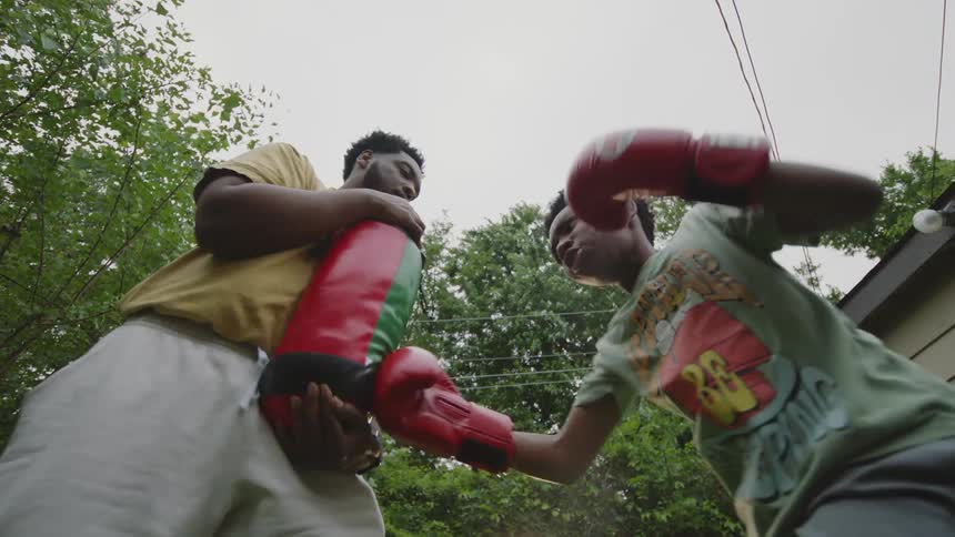 A father holds a punching bag for his son to practice boxing in their backyard in slow motion