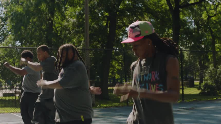 Four talented male street dancers showcase their dynamic, synchronized hip-hop routine on a sunlit basketball court in a park