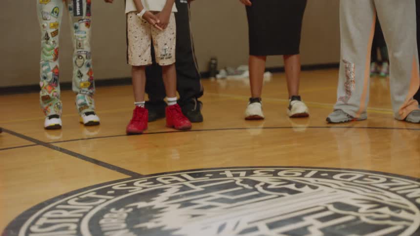 A close-up of a dancer's feet in sneakers showing off fast footwork moves on an indoor basketball court