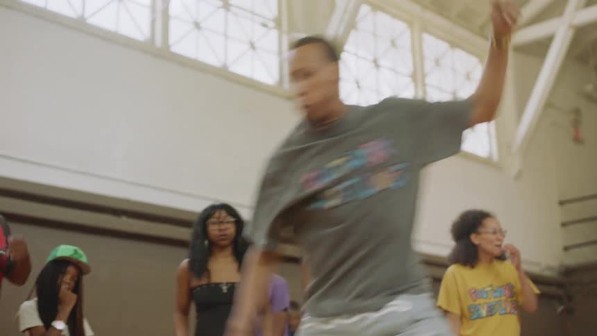 A man performs an impressive footwork dance routine in slow motion for a crowd in a gymnasium