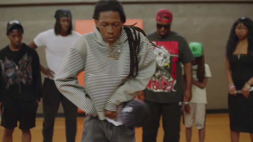 A talented young man with dreadlocks performs an energetic hip-hop krump dance for a crowd in a gymnasium