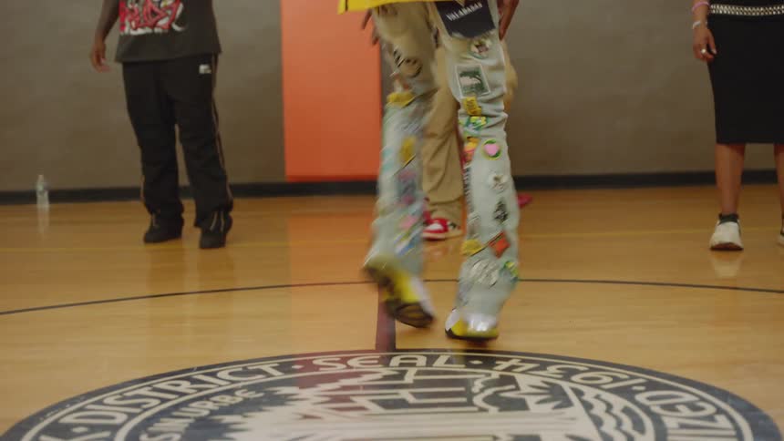 A skillful dancer with long dreadlocks showcases impressive footwork on a Chicago Park District gymnasium floor