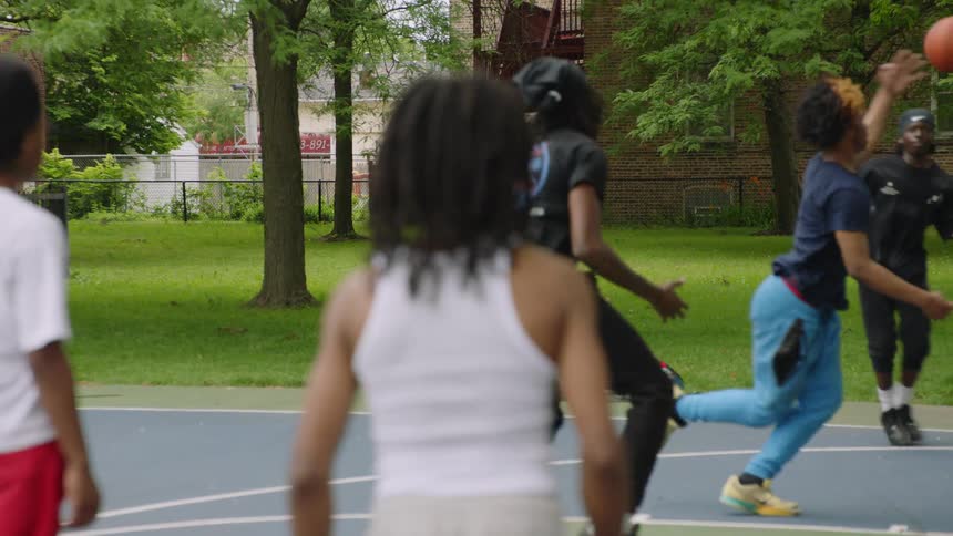 From behind a player, a group of young Black friends play a competitive game of basketball in slow motion