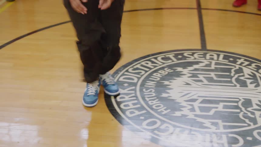 A talented female dancer performs energetic and intricate footwork in slow motion in a Chicago gymnasium while a crowd watches