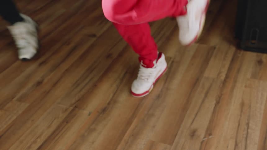 A young boy with wireless earbuds dances energetically in his room, with the camera tilting down to focus on his fancy footwork