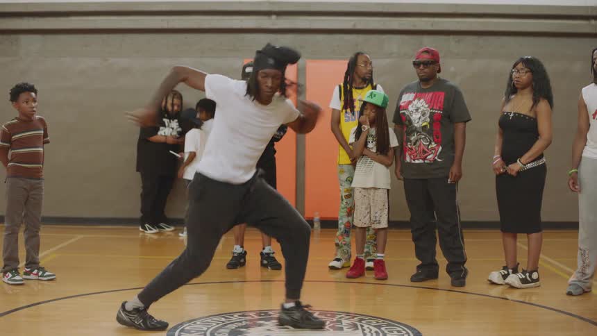 A talented young man shows off his energetic hip-hop dance moves for a crowd of spectators in a gymnasium