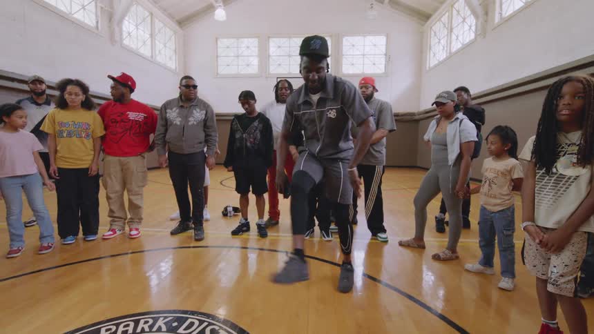 A man showcases his impressive and energetic footwork dancing in slow motion for a captivated crowd inside a gymnasium