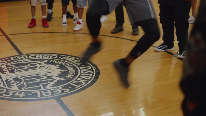 An athletic dancer performs an energetic Chicago Footwork routine on a gymnasium floor as a group of adults and children watch