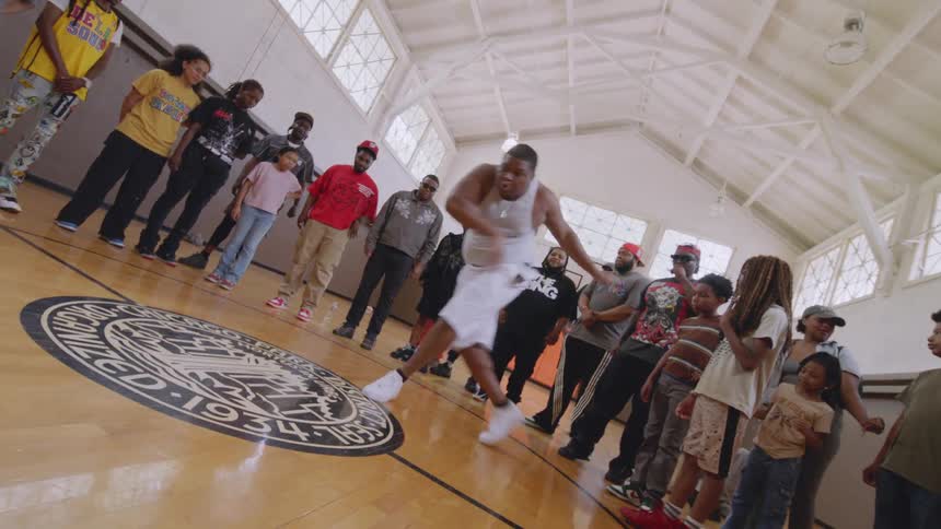 A talented dancer performs an energetic and expressive krump routine for an attentive crowd in a gymnasium dance circle