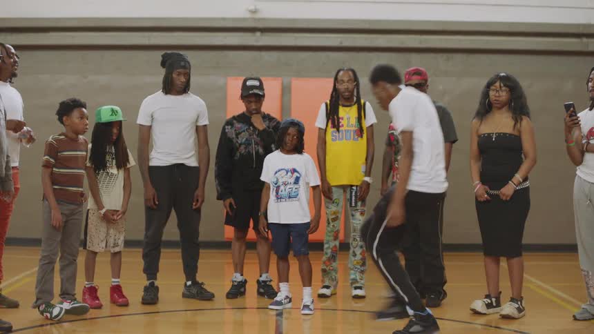 A young man showcases his intricate Jookin' dance moves to an attentive crowd of family and friends on an indoor basketball court