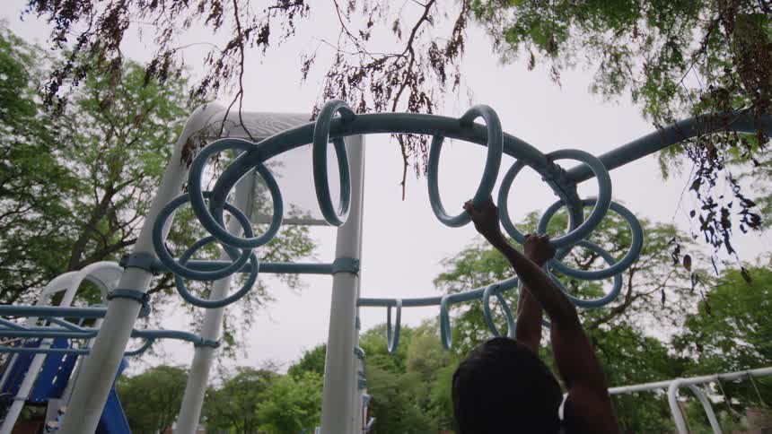 A muscular person with dreadlocks does pull-ups on the monkey bars at an outdoor park
