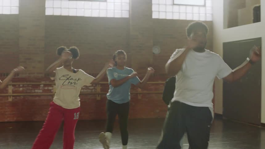 Young adult dancers practice a synchronized hip-hop choreography in a brightly lit studio