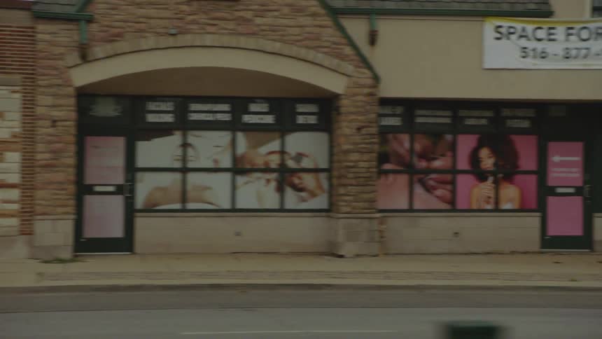 A slow-motion tracking shot of various storefronts and buildings on a quiet urban street during an overcast day