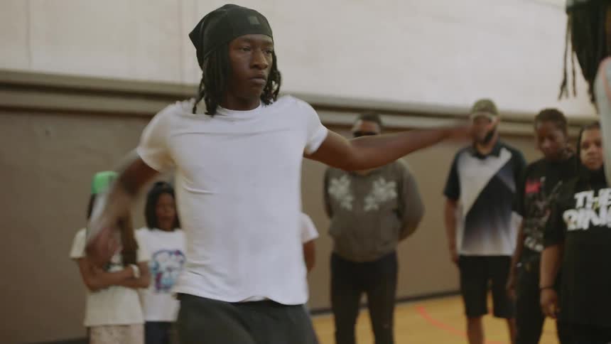 A talented young dancer performs a high-energy, intricate footwork routine in slow motion on a Chicago gymnasium floor as a crowd watches