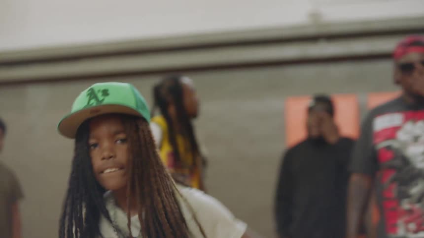 Energetic young boy with long dreadlocks dances with swagger in a gym, with a tilt down to his stylish red sneakers