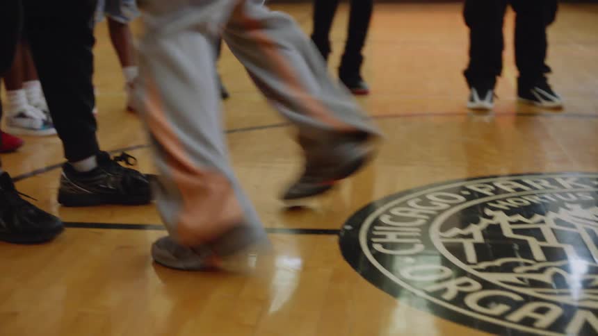 A dancer's feet move with speed and precision, performing Chicago Footwork on a basketball court during an intense dance battle