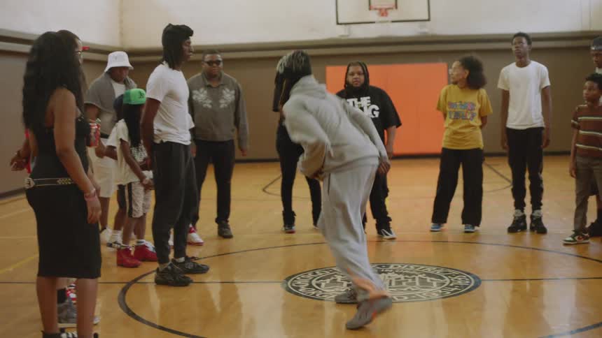 A talented dancer performs energetic krump moves for an audience in a cypher on an indoor basketball court