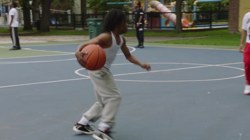 A young man skillfully dribbles past a defender and makes a successful jump shot on an outdoor basketball court in slow motion