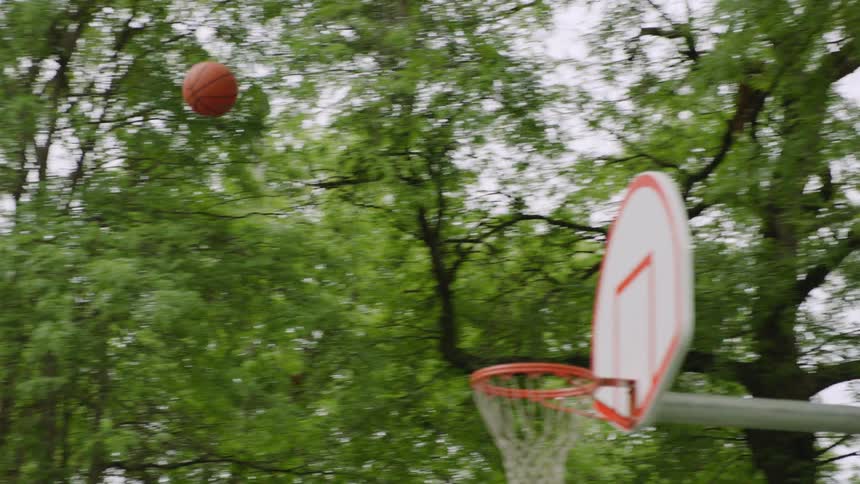 A basketball player makes a perfect shot in slow motion on an outdoor court, sinking the ball through the net