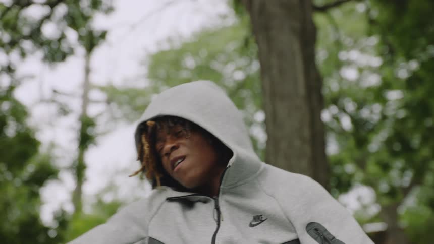 Slow-motion shot of a thoughtful young person with dreadlocks in a hoodie relaxing in a wheelchair outdoors in a park