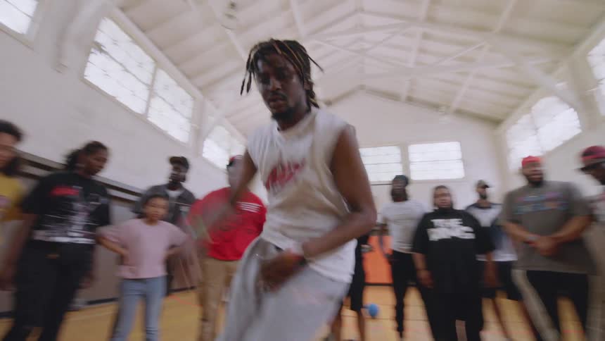 A talented dancer performs an energetic and fast-paced footwork routine for a crowd of onlookers in a community gymnasium