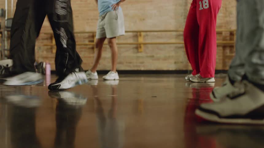 A low-angle shot captures a hip-hop dancer's intricate footwork on a reflective studio floor