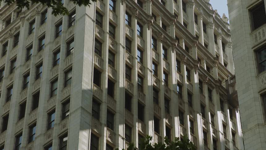 A low-angle shot slowly pans down the ornate facade of a classical stone building in a city on a sunny day