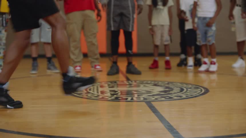 Close-up on the feet of a dancer performing intricate footwork on a basketball court as a crowd watches