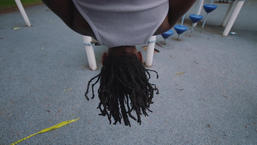 A young person with dreadlocks hangs upside down on playground equipment, their hair swaying gently