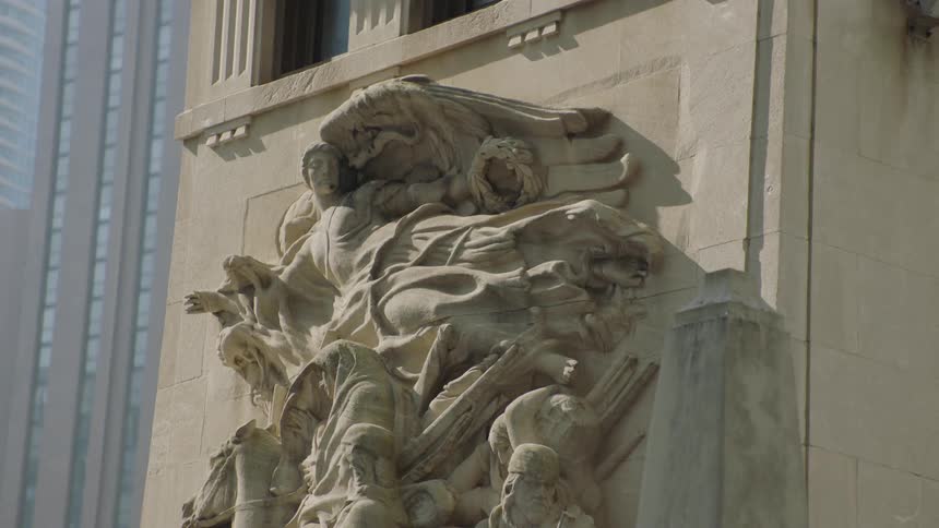 An intricate historical bas-relief sculpture is carved into the side of a classical city building