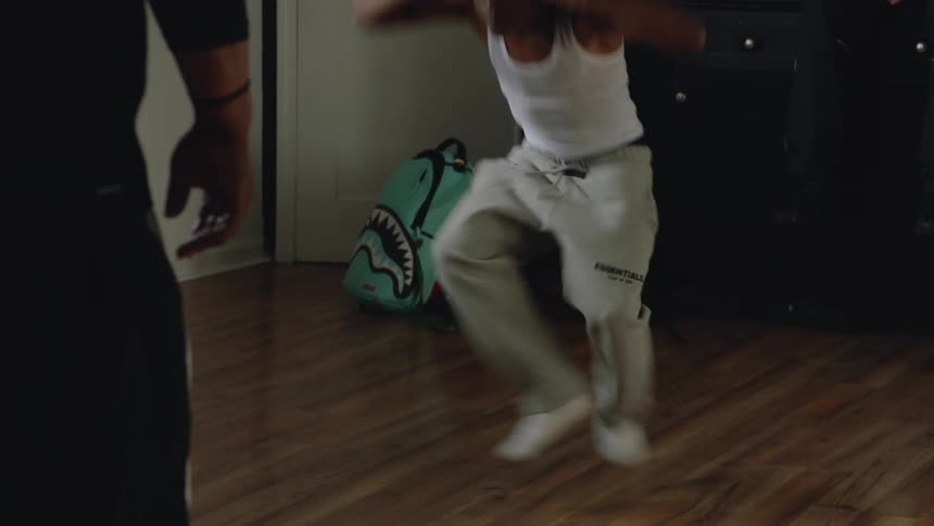 A young man with headphones performs an energetic and intense krump dance in slow motion for his friends indoors