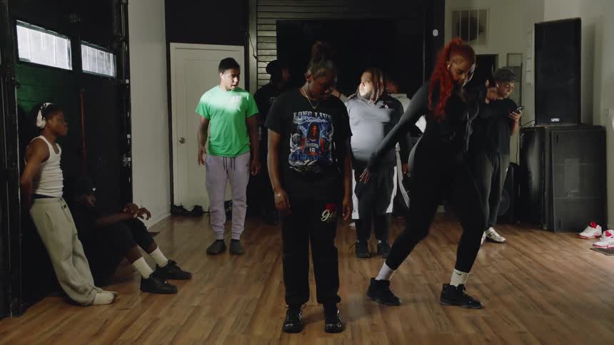 A group of young adults practice hip-hop dance moves together in a studio during a rehearsal