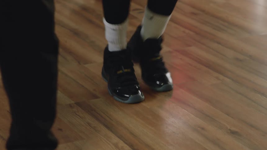 Close-up tilt down of a woman in workout clothes and earbuds exercising indoors, showing her determined face and then her feet in motion