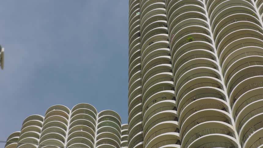 A static low-angle view of the iconic Marina City towers in Chicago, featuring their distinctive corn-cob-like curved balconies against a blue sky