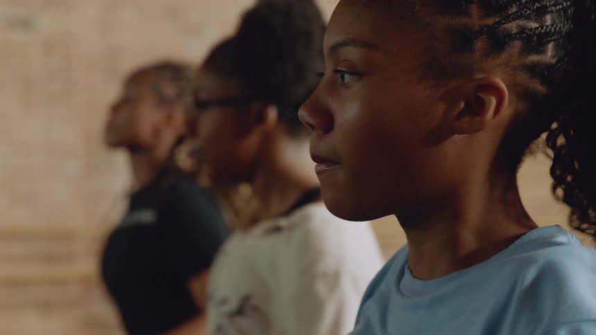 A close-up profile shot of determined young Black girls with braided hair performing synchronized dance moves in a line