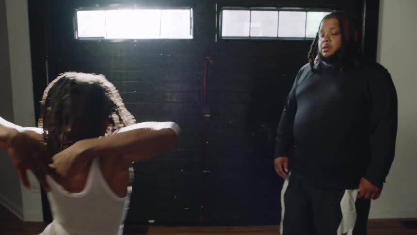 A father coaches his determined young son as he practices an energetic dance in a dramatically lit room in slow motion