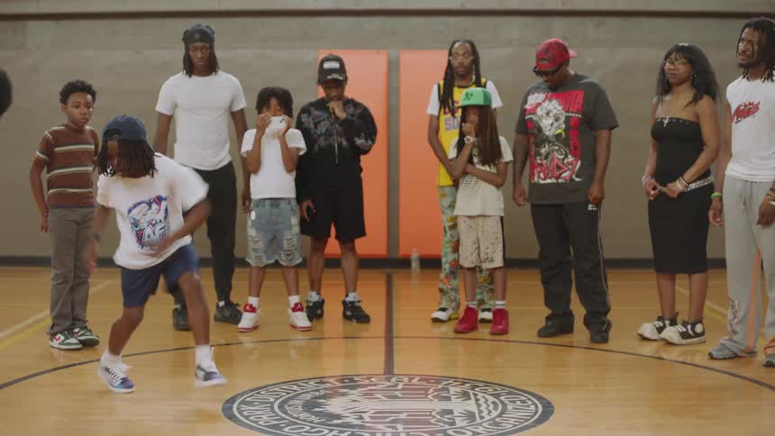 A talented young boy shows off his impressive hip-hop dance moves for a supportive crowd in a gymnasium