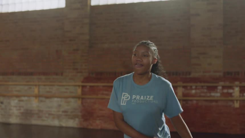 An energetic young woman practices a hip-hop dance routine in a sunlit studio, with the slow-motion camera tilting down to her intricate footwork