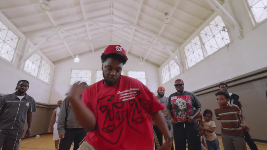 A skilled dancer showcases his energetic footwork and expressive moves in the center of a dance circle on a Chicago basketball court
