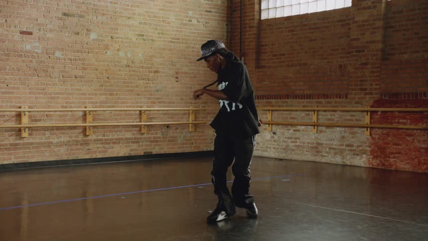 A skilled male hip-hop dancer showcases his fluid moves in slow motion inside an urban dance studio with a brick wall