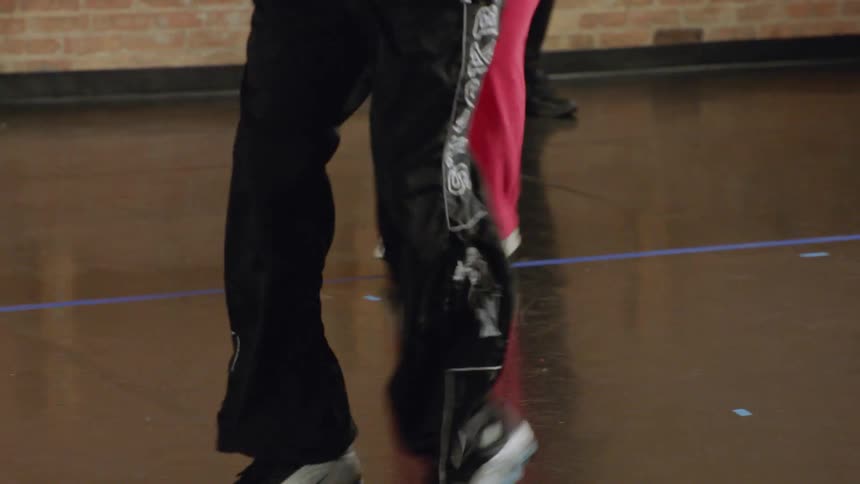 A slow-motion tilt down from a dancer's face reveals the intricate footwork of a line of dancers practicing in a studio