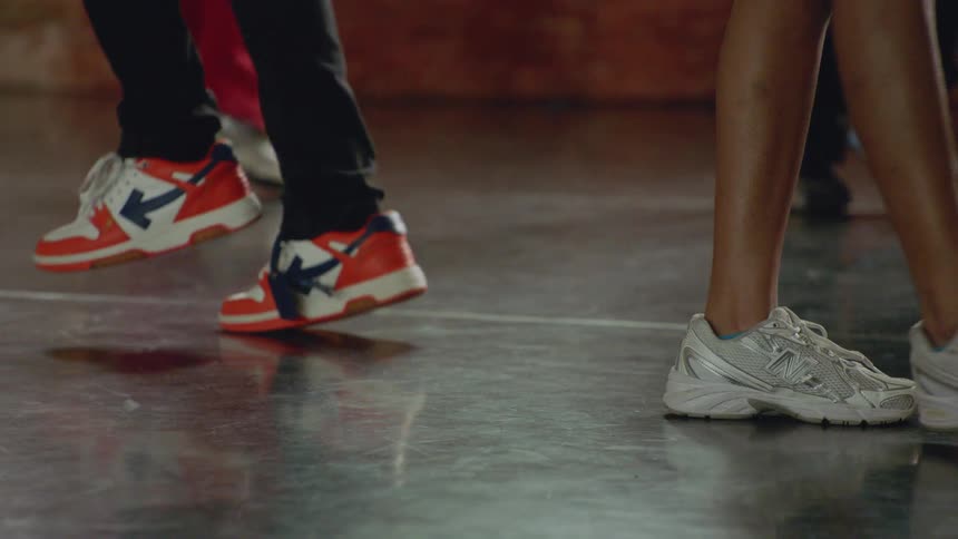 Slow motion, low angle shot of dancers' feet in sneakers moving in unison on a reflective floor