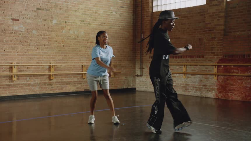 Two dancers practice synchronized hip-hop footwork in slow motion inside a dance studio