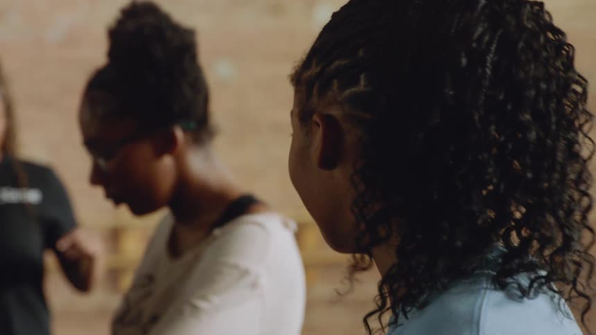 A young black woman with her hair in a braided ponytail listens attentively during a group workshop or class in slow motion