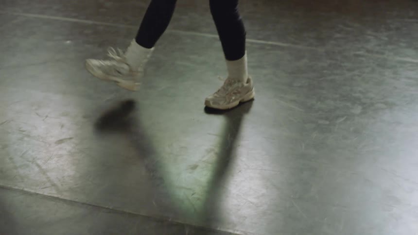 A close-up shot focuses on the energetic and rhythmic footwork of a dancer wearing sneakers in a studio