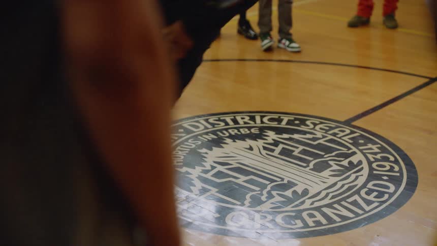 Slow motion shot of a talented young man performing intricate hip-hop dance moves while surrounded by a crowd in a gymnasium