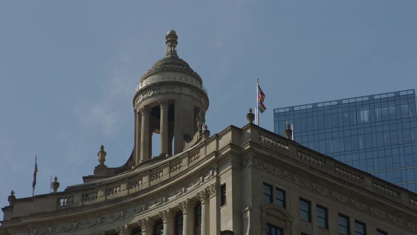 A rainbow Pride flag and an American flag wave proudly from the roof of an ornate classical building in a city